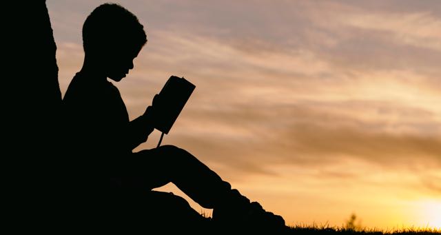 silhouette of a boy reading a book at sunset