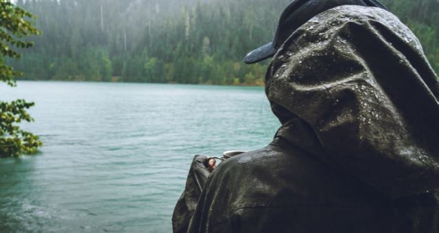 men in a hoody holding a ta cup overlooking lake