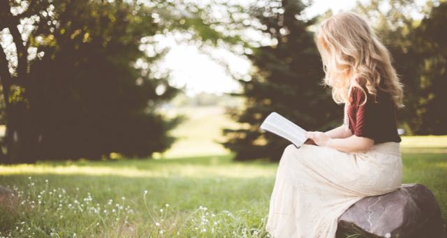a blond girl in white dress reading a book in the park