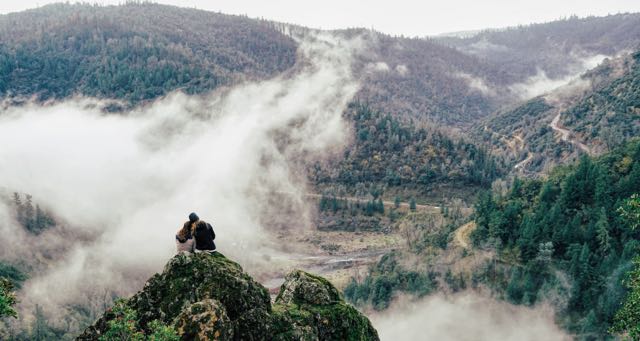 couple sitting on a rock overlooking a foggy valley